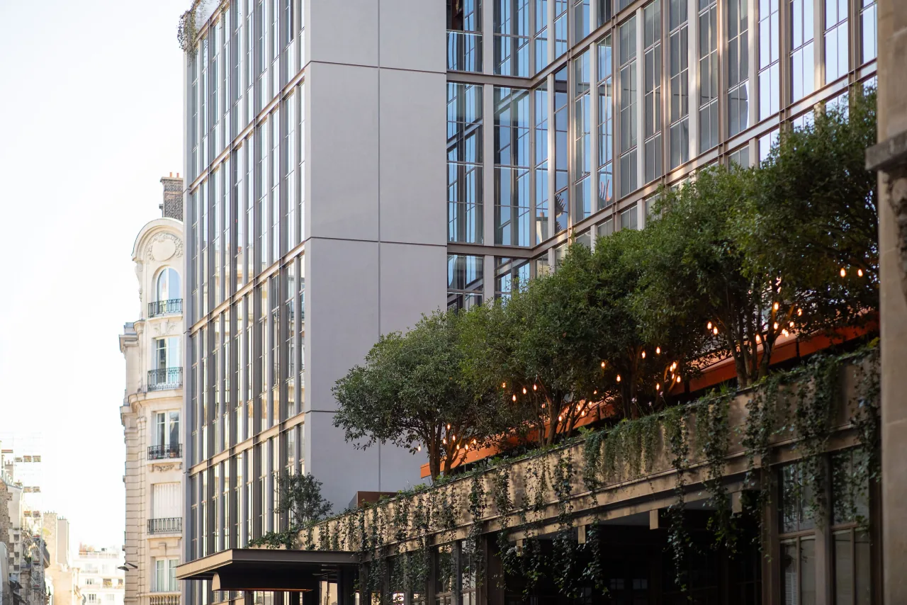 A glass façade with a planted terrace of trees and garlands, beside a Haussmann building