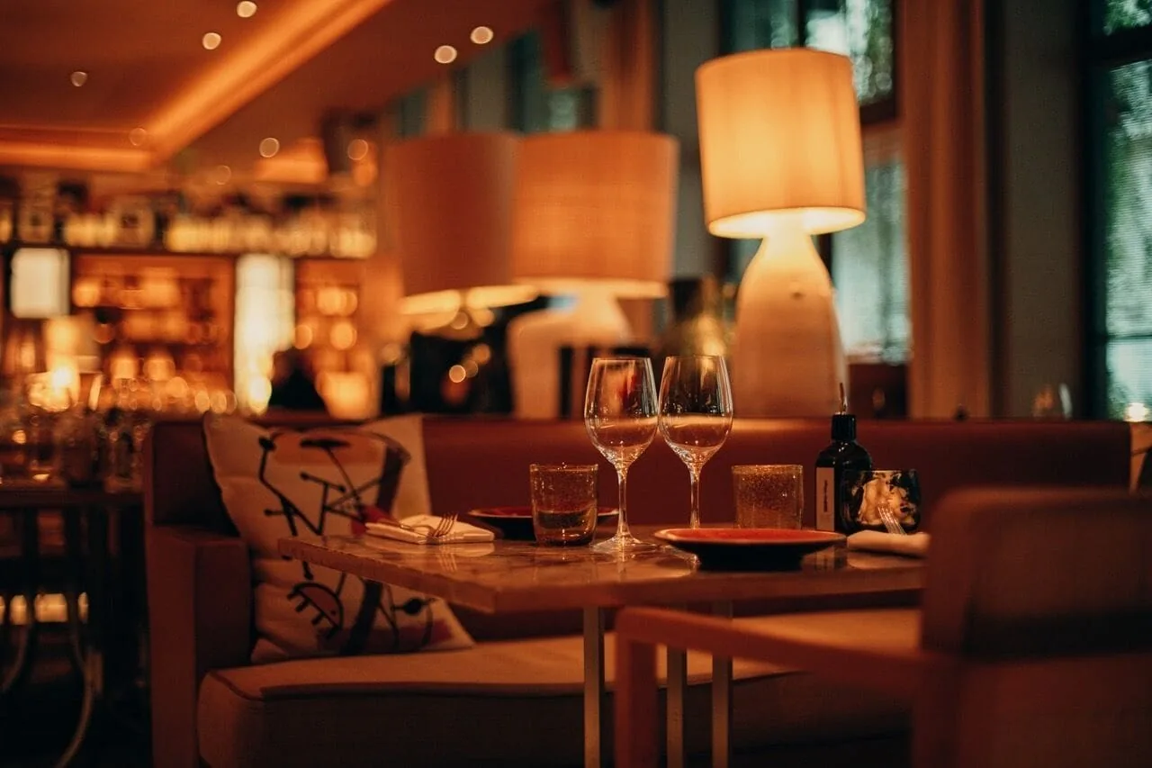 A bar at night in warm light, lamps and bottles on shelves