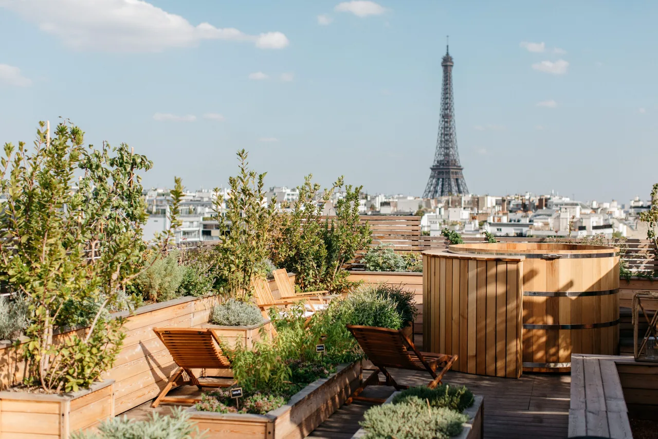 A rooftop garden with planters, wooden deckchairs and a wooden bath, the Eiffel Tower behind