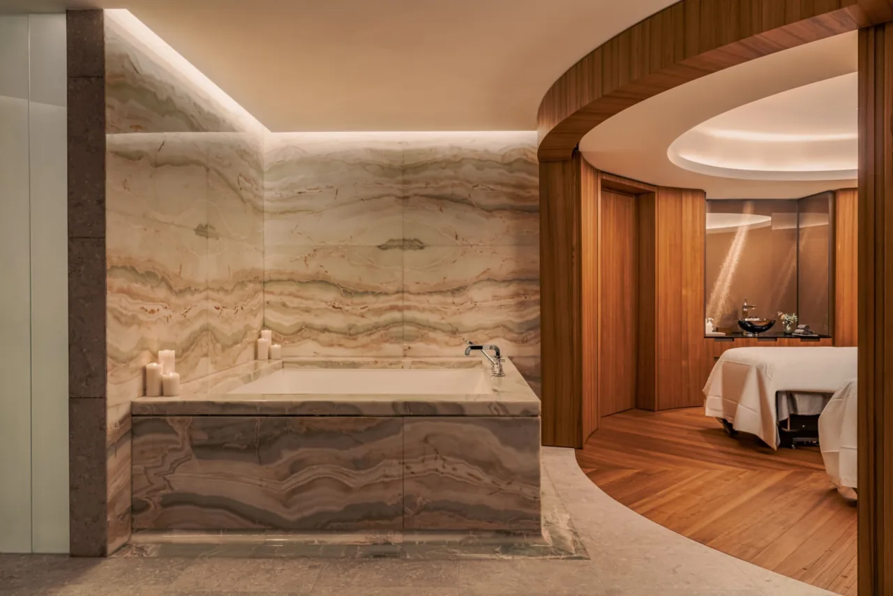 A treatment room with a veined stone bathtub and a massage table in a rounded alcove