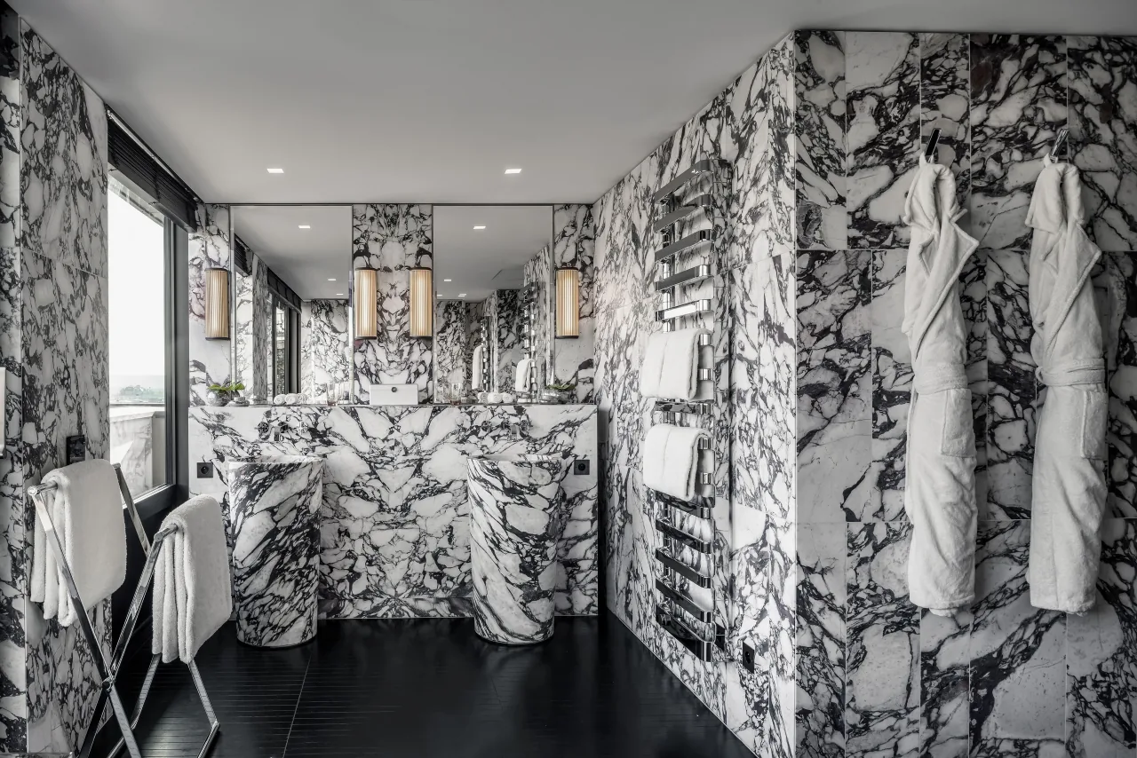 A bathroom clad in black-and-white veined marble, with a bathtub and two bathrobes