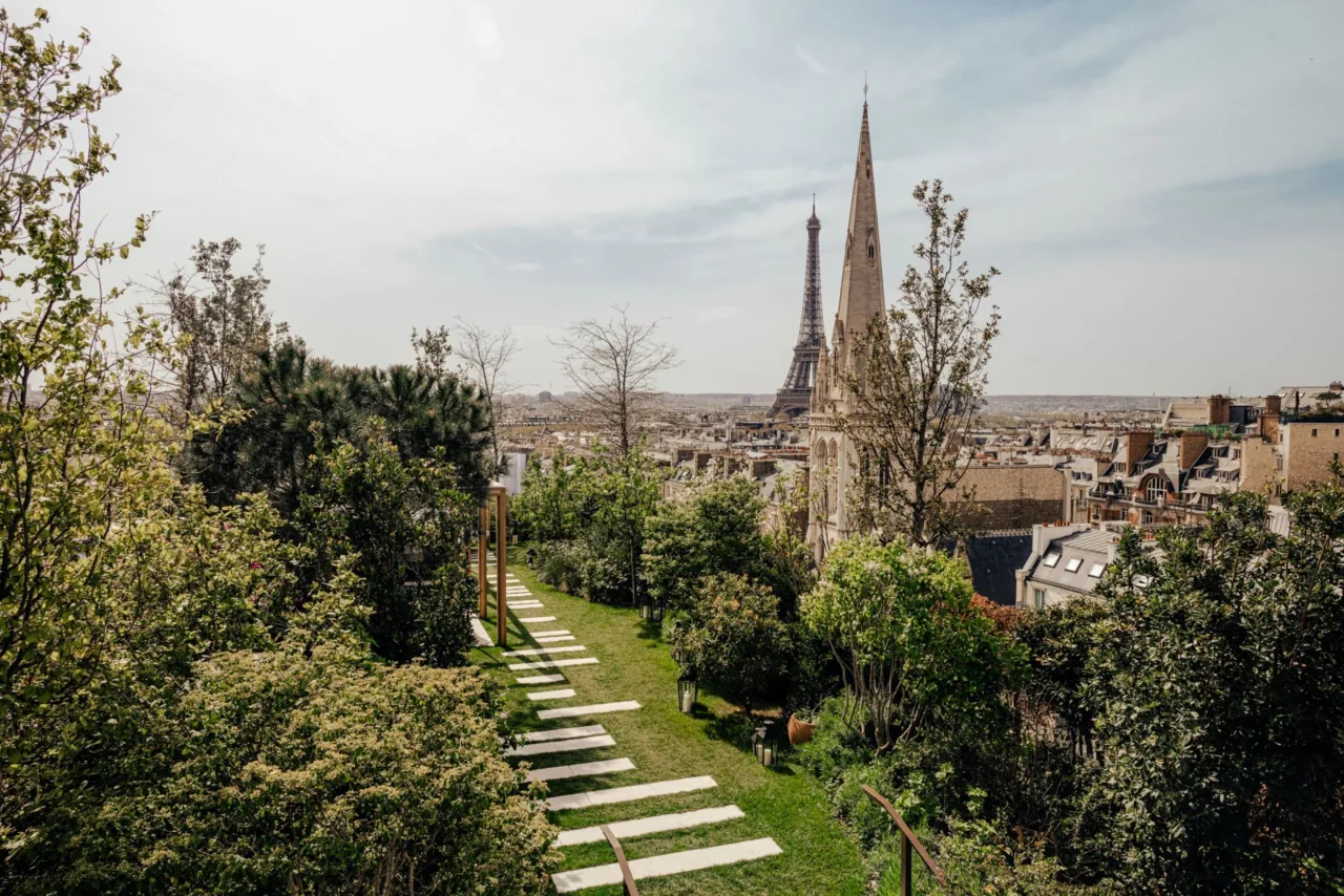 A terrace garden with trees and stepping stones, the Eiffel Tower and a church spire in the distance