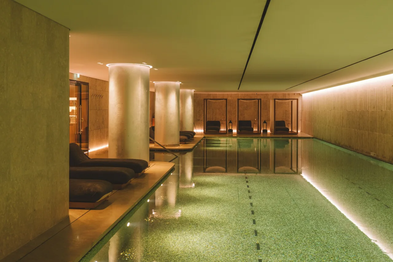 A pool lined with stone columns and loungers, in warm light