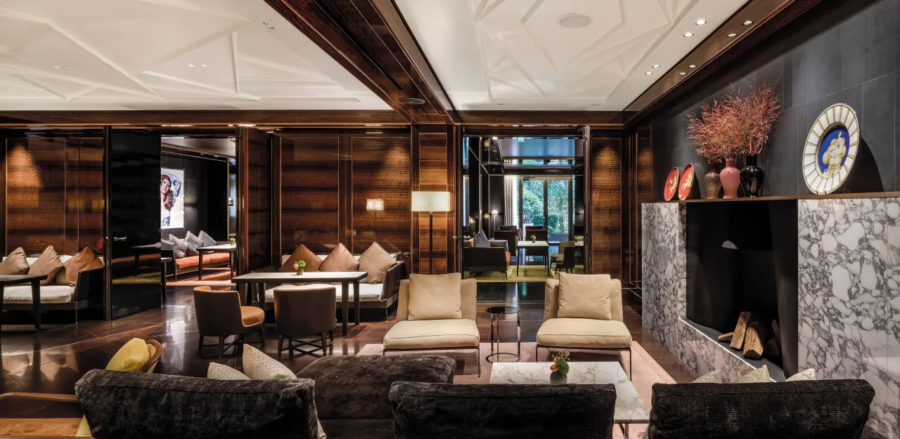 A wood-panelled lounge with armchairs, low tables and a marble fireplace