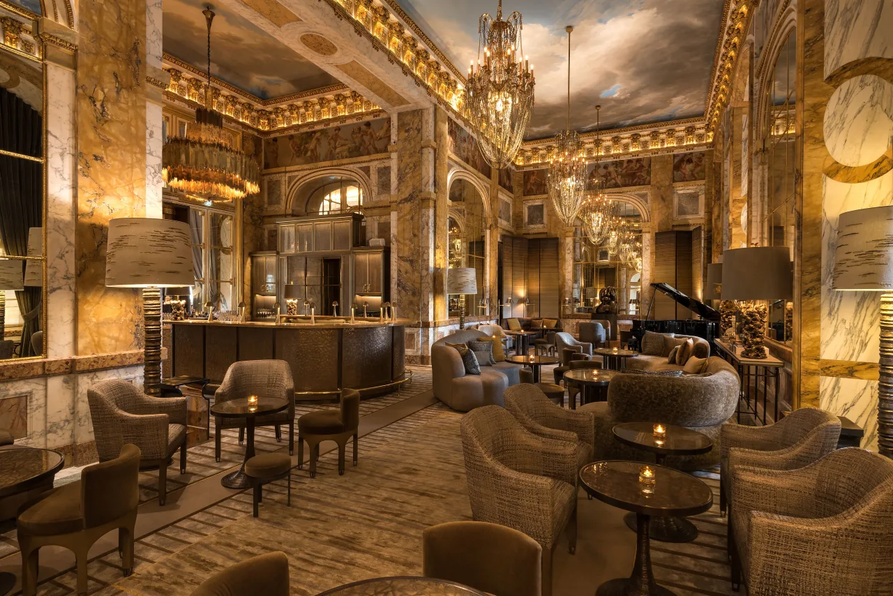 Un bar sous un plafond peint et doré, des fauteuils, des tables basses et un piano à queue