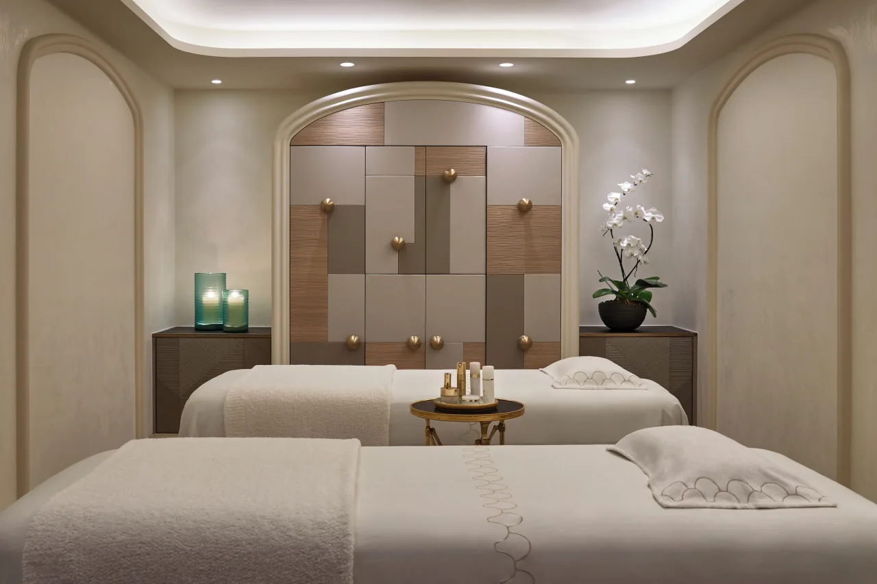 Une cabine de soins à deux tables de massage, lumière douce et panneau de bois dans l’alcôve