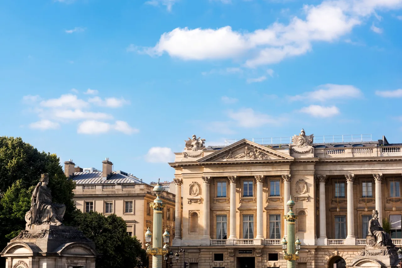 La façade de pierre à colonnade sur la place de la Concorde, sous un ciel bleu, une statue au premier plan