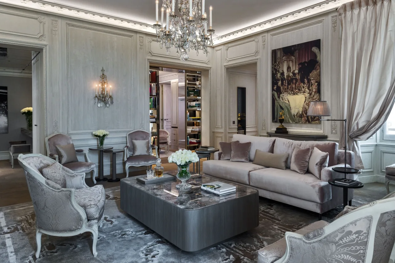 Un salon aux tons gris, un lustre de cristal, un grand tableau, des fauteuils et une table basse