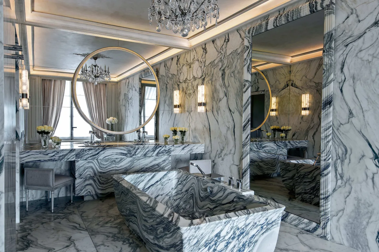 Une salle de bains en marbre veiné gris et blanc, une baignoire îlot et un miroir rond