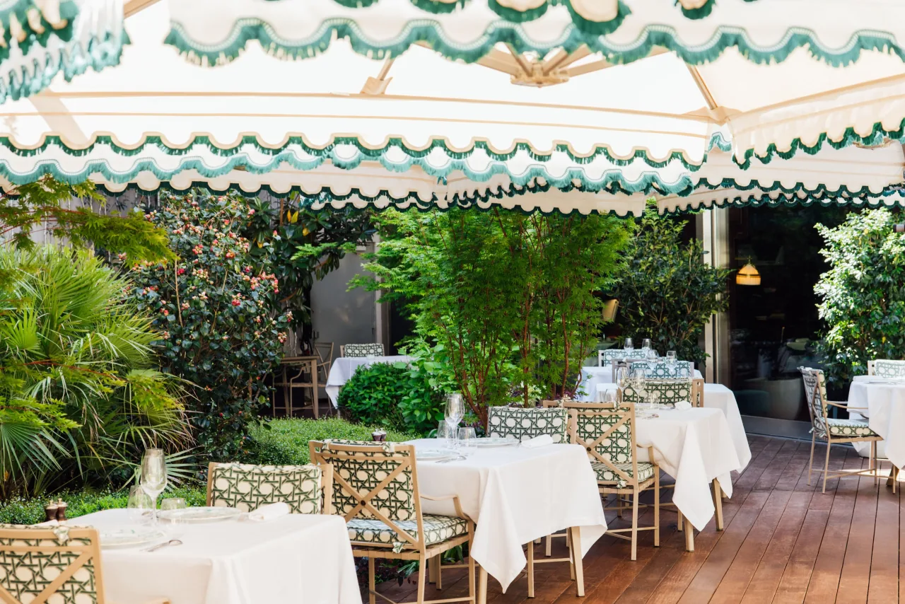 Une terrasse aux tables dressées sous un store festonné vert et blanc, entre des arbres et des bambous