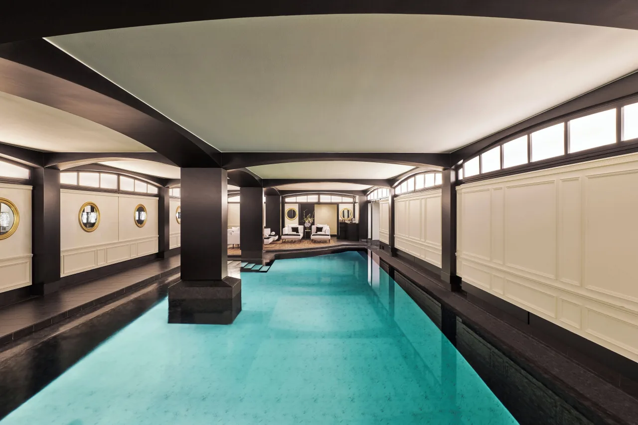 Une longue piscine intérieure à l’eau turquoise, des colonnes sombres et des murs lambrissés clairs