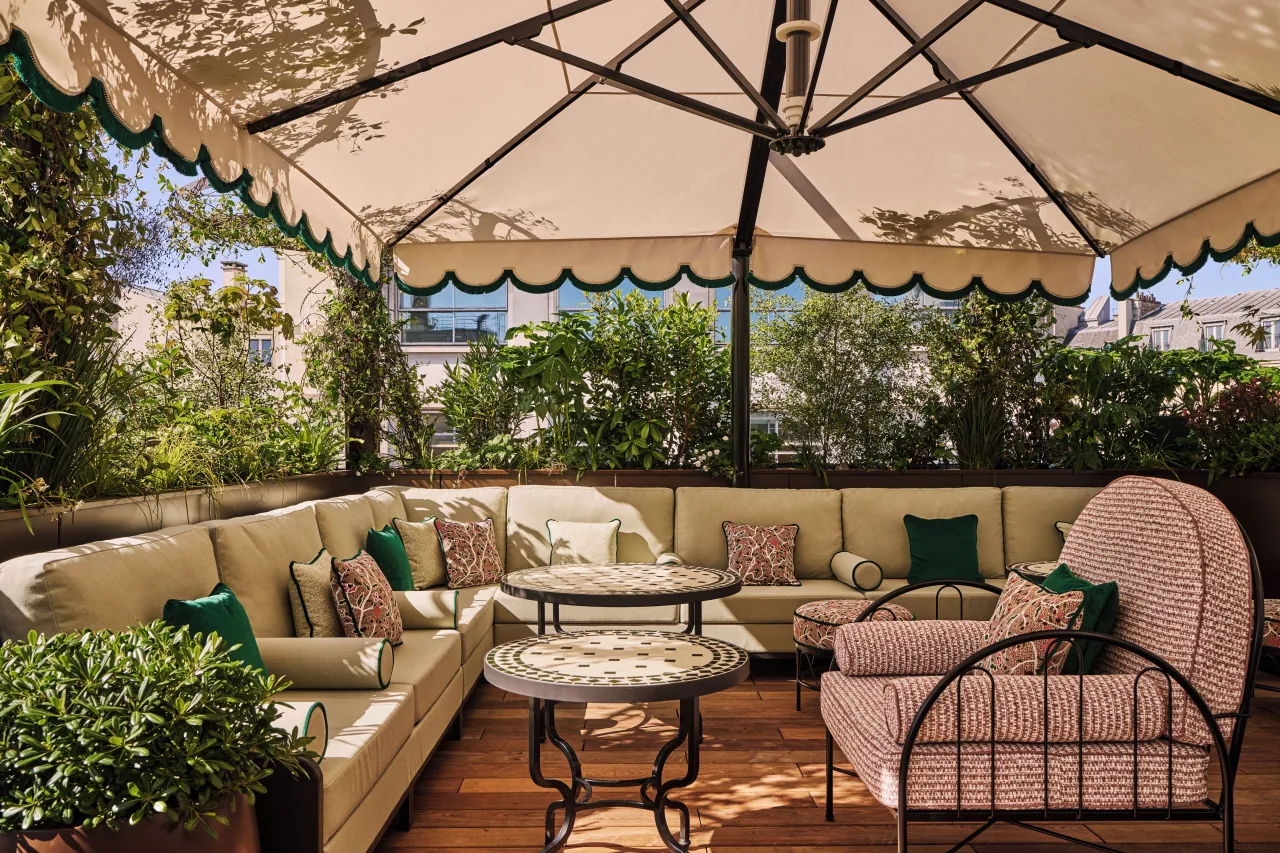 Une terrasse, des canapés et des tables basses sous de grands parasols, entourés de plantes