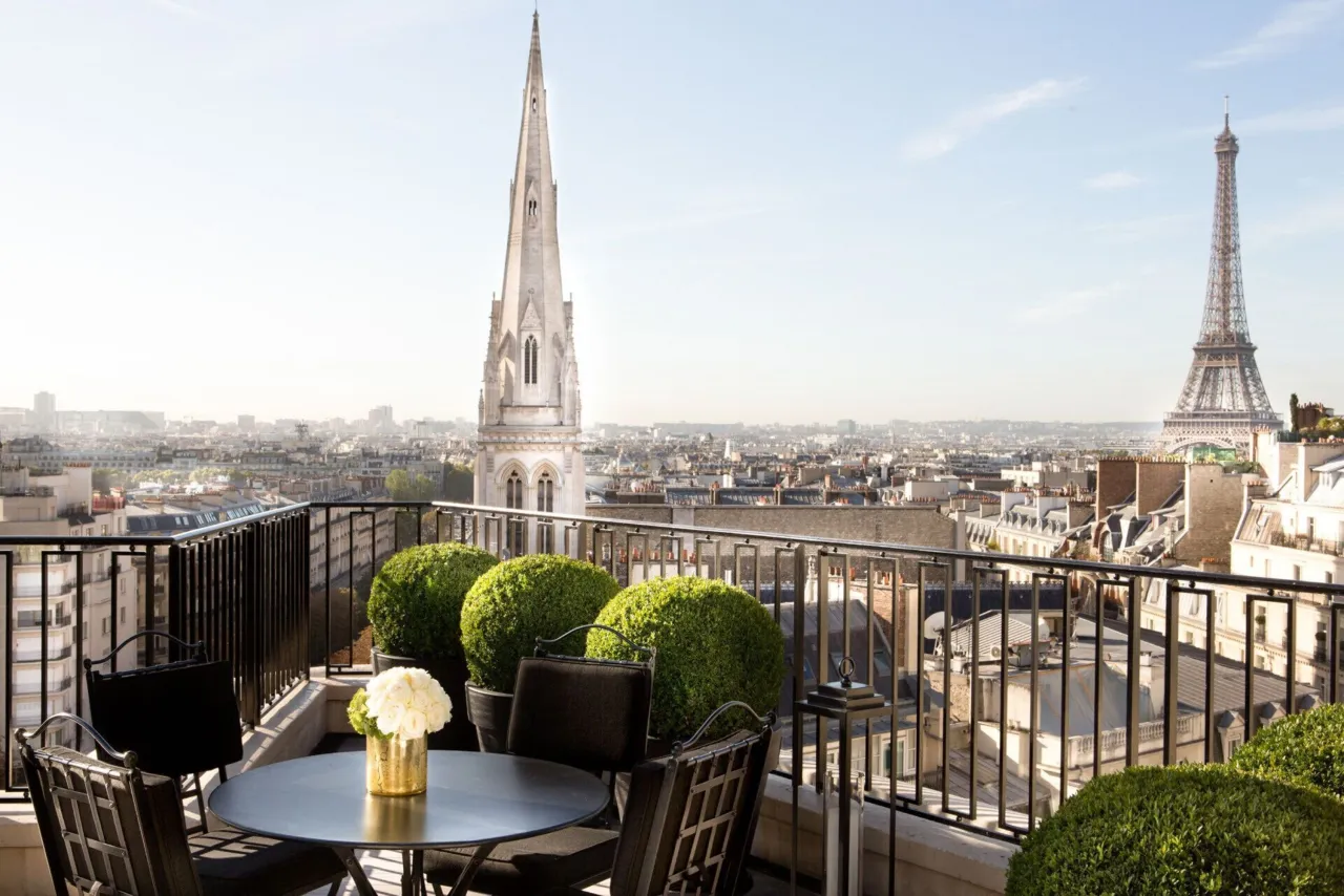 Une table sur une terrasse aux buis taillés, une flèche d’église à gauche et la tour Eiffel à droite