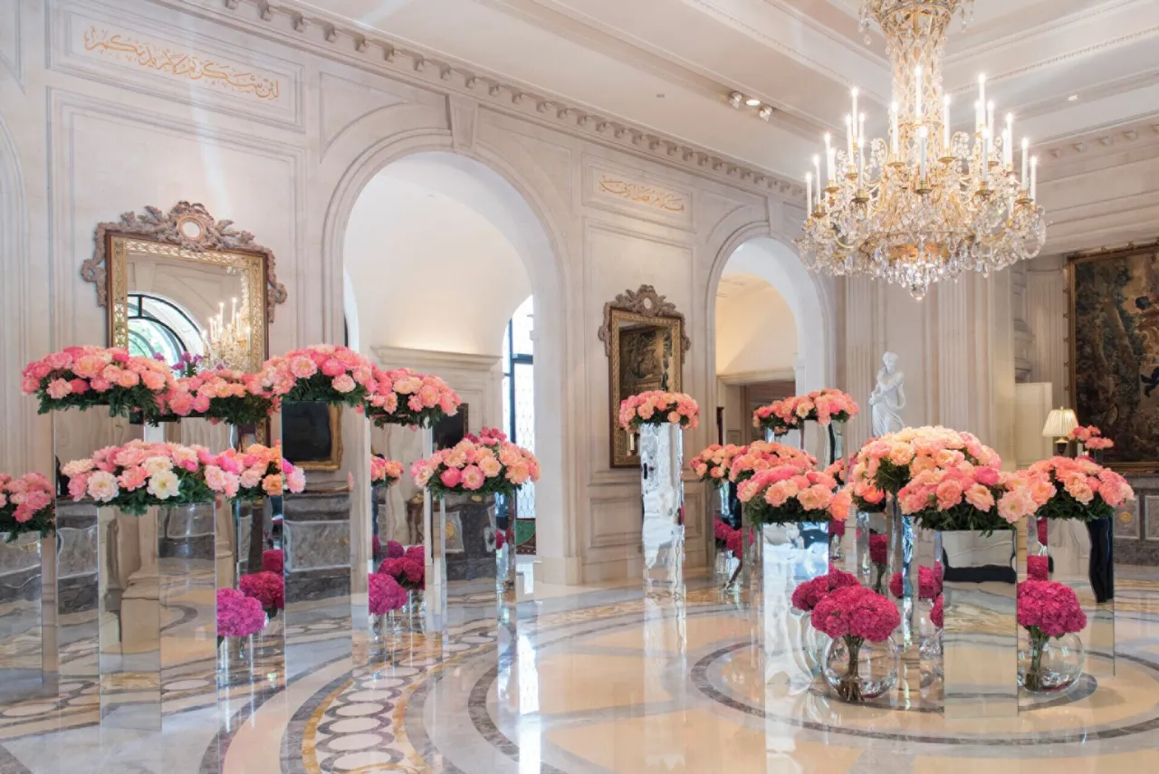 Un hall de marbre à arcades, lustre de cristal et hauts vases de verre garnis de roses