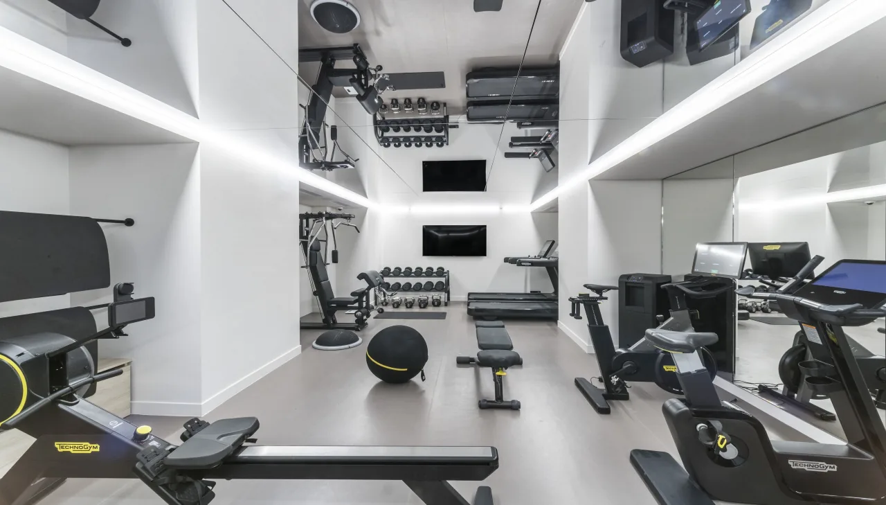 Une salle de sport blanche, un rameur, des vélos, des haltères et des murs couverts de miroirs