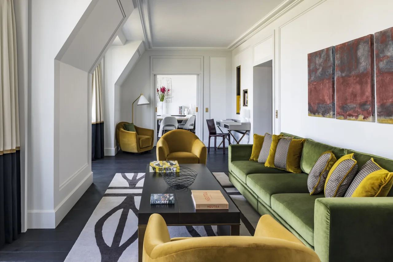 Un salon au canapé vert et aux fauteuils ocre, une table de salle à manger et un grand tableau