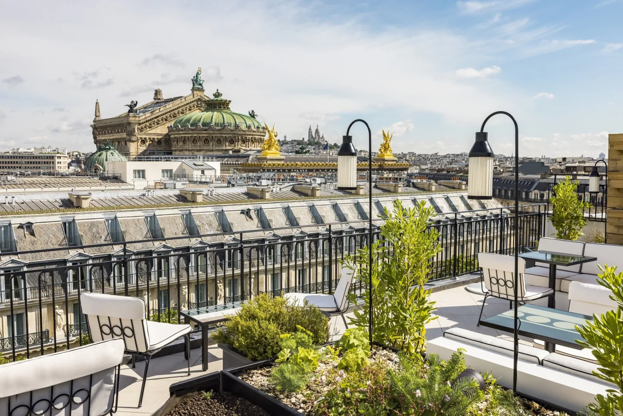 Une terrasse plantée sur les toits, avec des lanternes et des chaises, le dôme vert de l’Opéra Garnier au loin