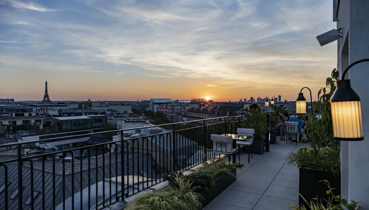 Une terrasse sur les toits au coucher du soleil, une lanterne, la tour Eiffel à l’horizon