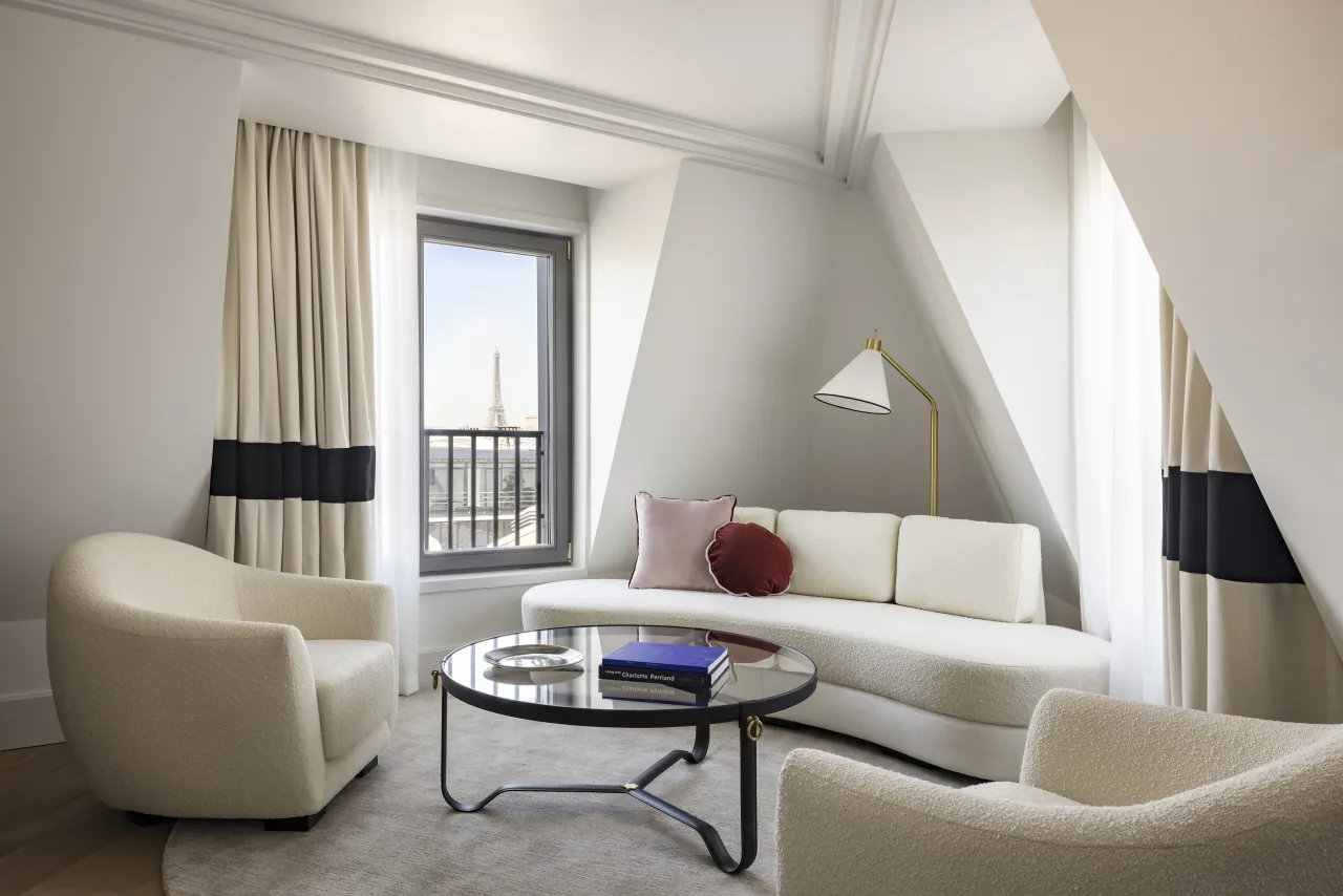 Un salon blanc aux fauteuils courbes et au canapé, la tour Eiffel au loin par la fenêtre