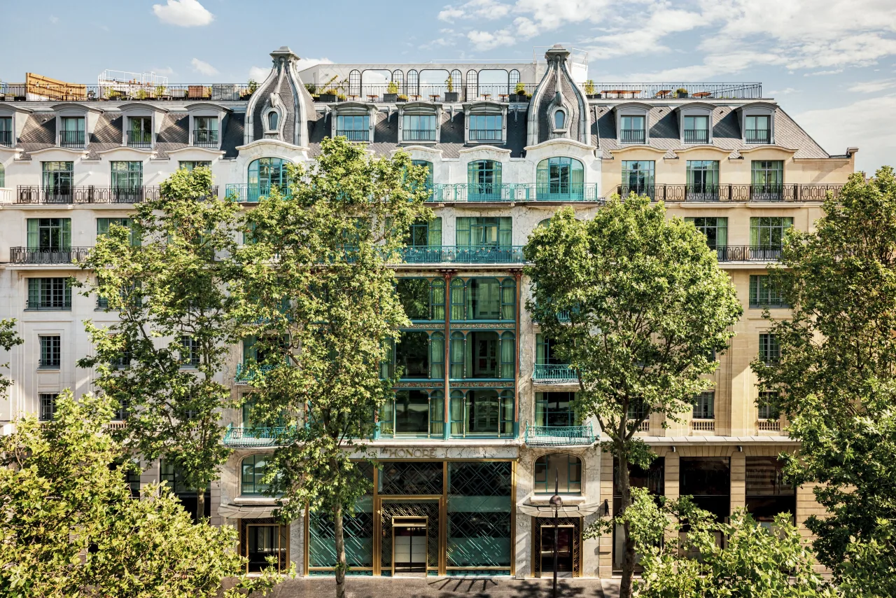 Une façade Art nouveau aux bow-windows turquoise et aux détails dorés, derrière des platanes