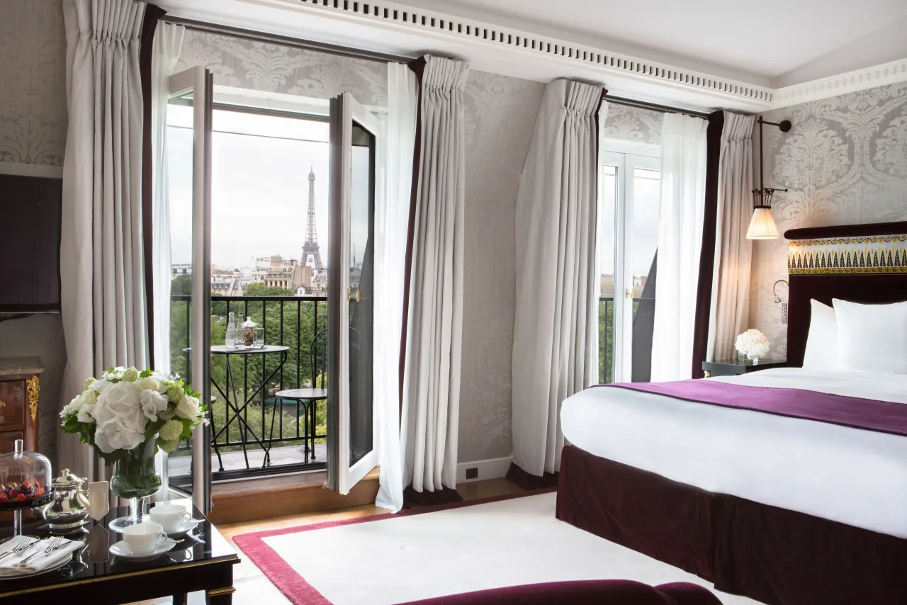 Un lit face à des portes-fenêtres ouvertes sur un balcon, les arbres et la tour Eiffel