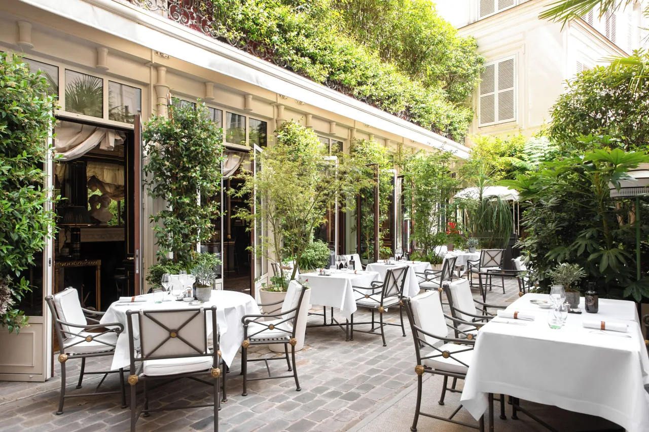 Un patio pavé, des tables nappées de blanc, des chaises de métal et des plantes grimpantes