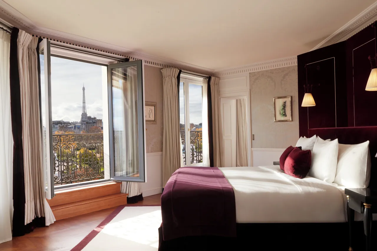 Un lit à tête de velours face à une fenêtre ouverte sur les arbres et la tour Eiffel