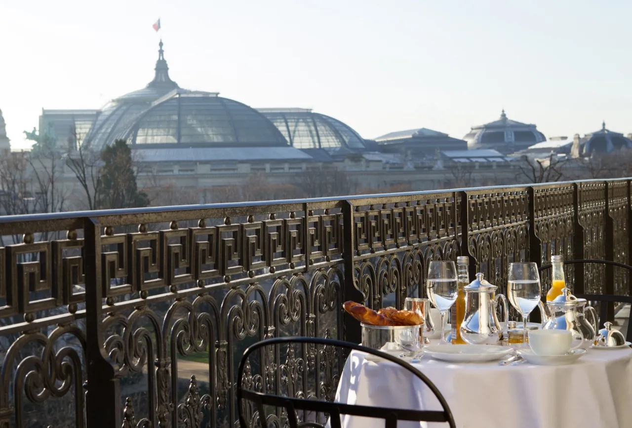 Une table de petit-déjeuner sur un balcon à la balustrade ouvragée, la verrière du Grand Palais au loin