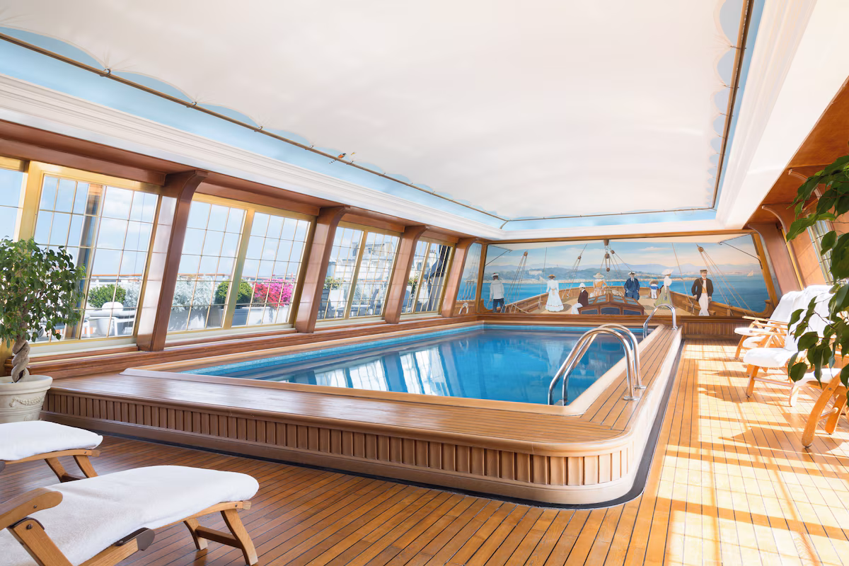La piscine intérieure du Bristol Paris, entourée de bois et de fenêtres, avec un décor de voiliers