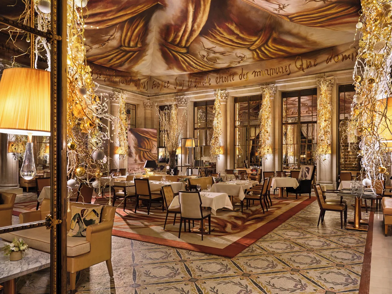 Un restaurant sous un vaste plafond de toile peinte, des tables, des fauteuils, des lampes et des lumières dans de hautes branches