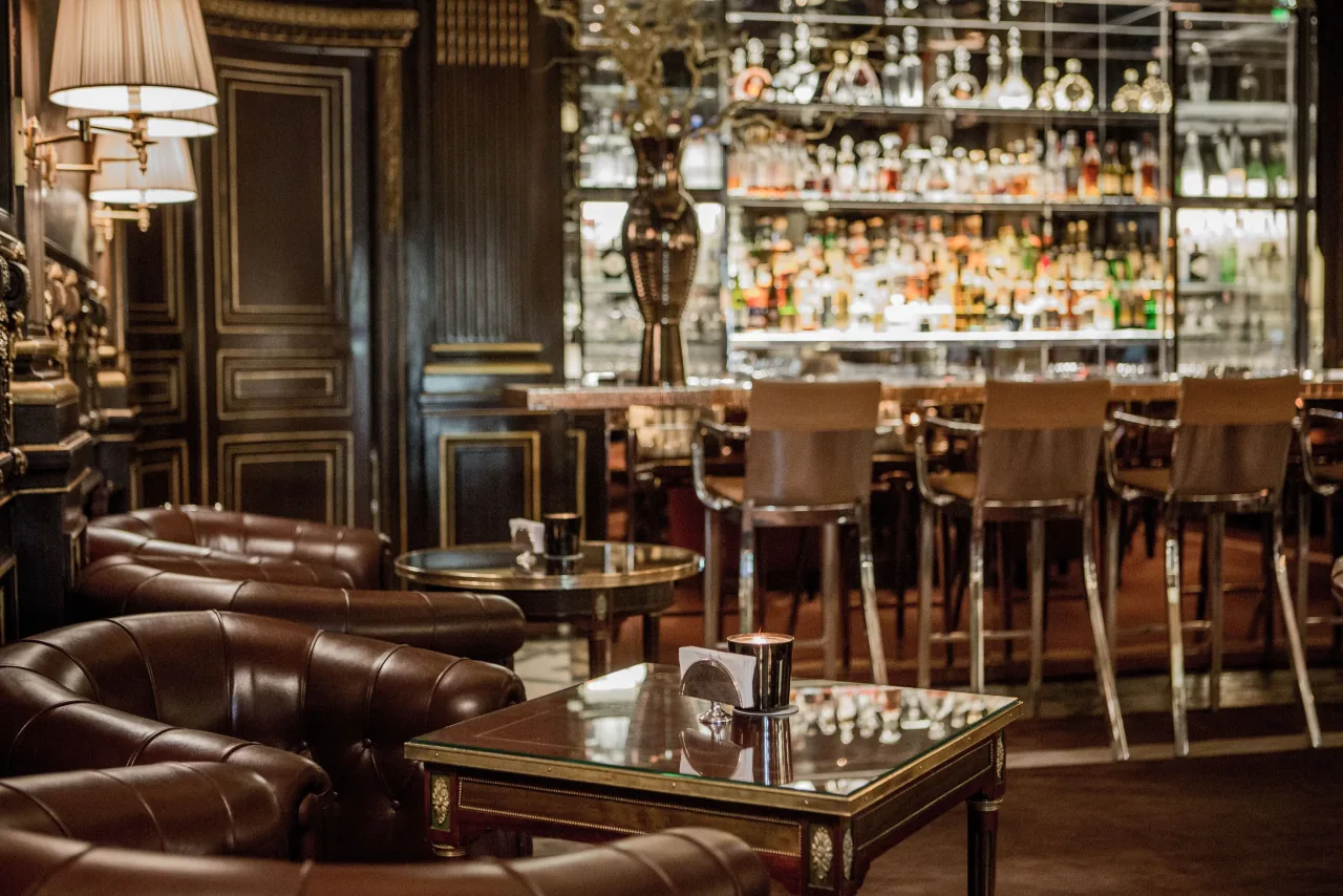 Un bar aux fauteuils club de cuir brun, des boiseries sombres, un comptoir de marbre et un mur de bouteilles éclairé