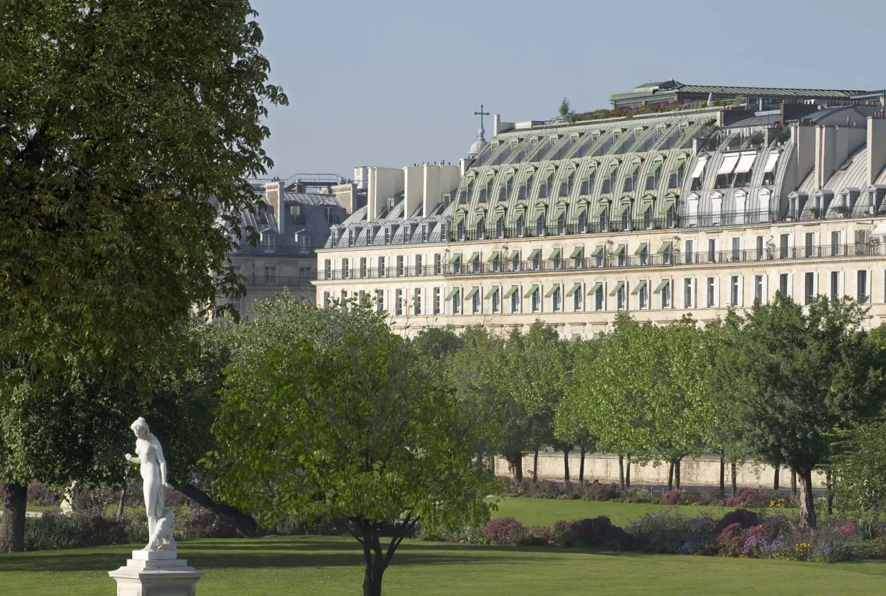 Une longue façade de pierre claire au toit mansardé d’ardoise verte, au-dessus des arbres du jardin des Tuileries, une statue blanche au premier plan
