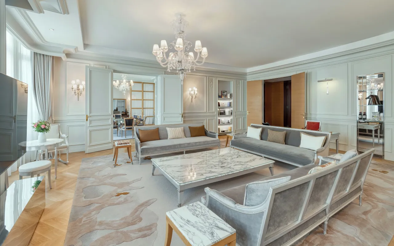 Le salon d’une suite, canapés gris clair, table basse en marbre et lustre de cristal