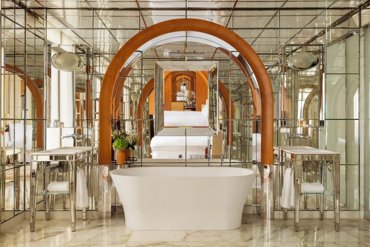 Une salle de bains aux murs de miroirs, baignoire îlot et arche de bois