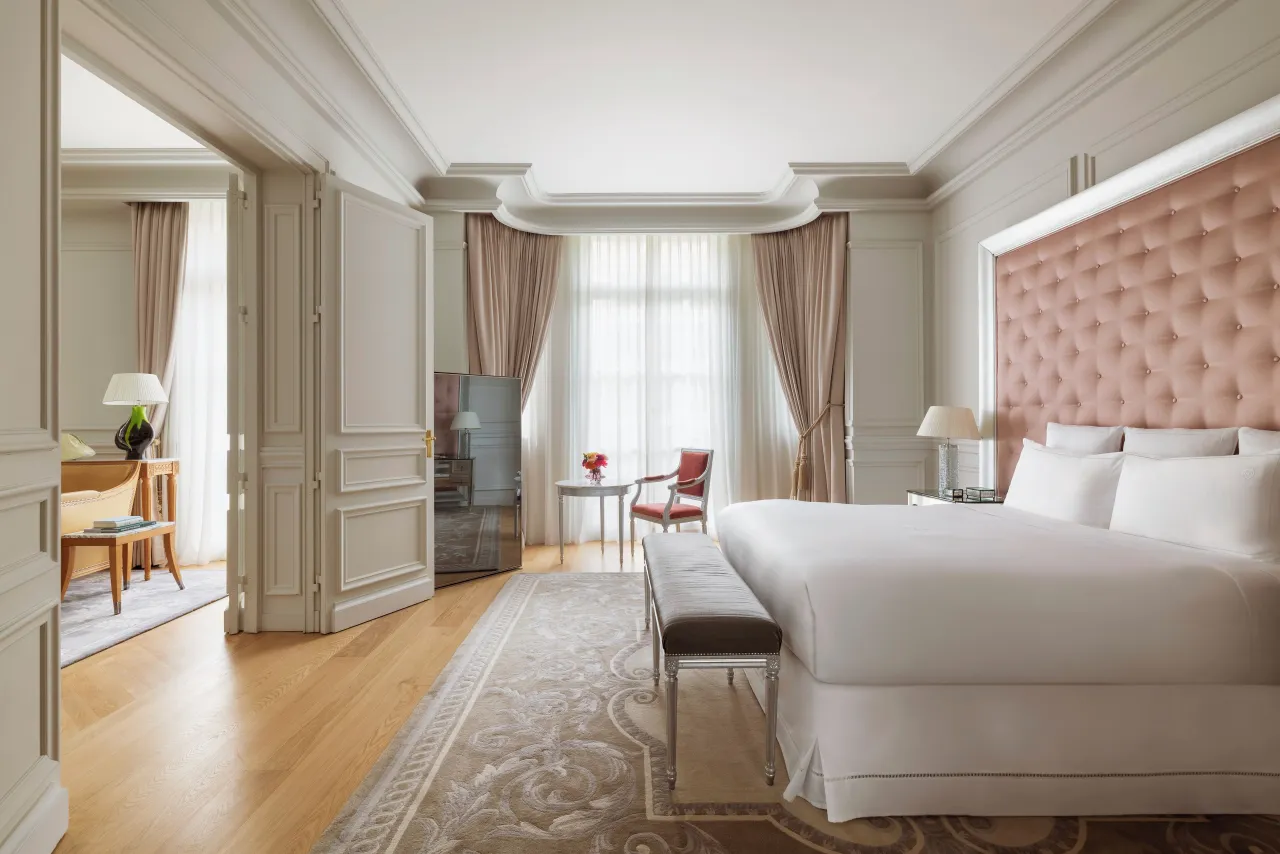 Une chambre à tête de lit capitonnée rose, grand lit blanc, banquette et parquet clair
