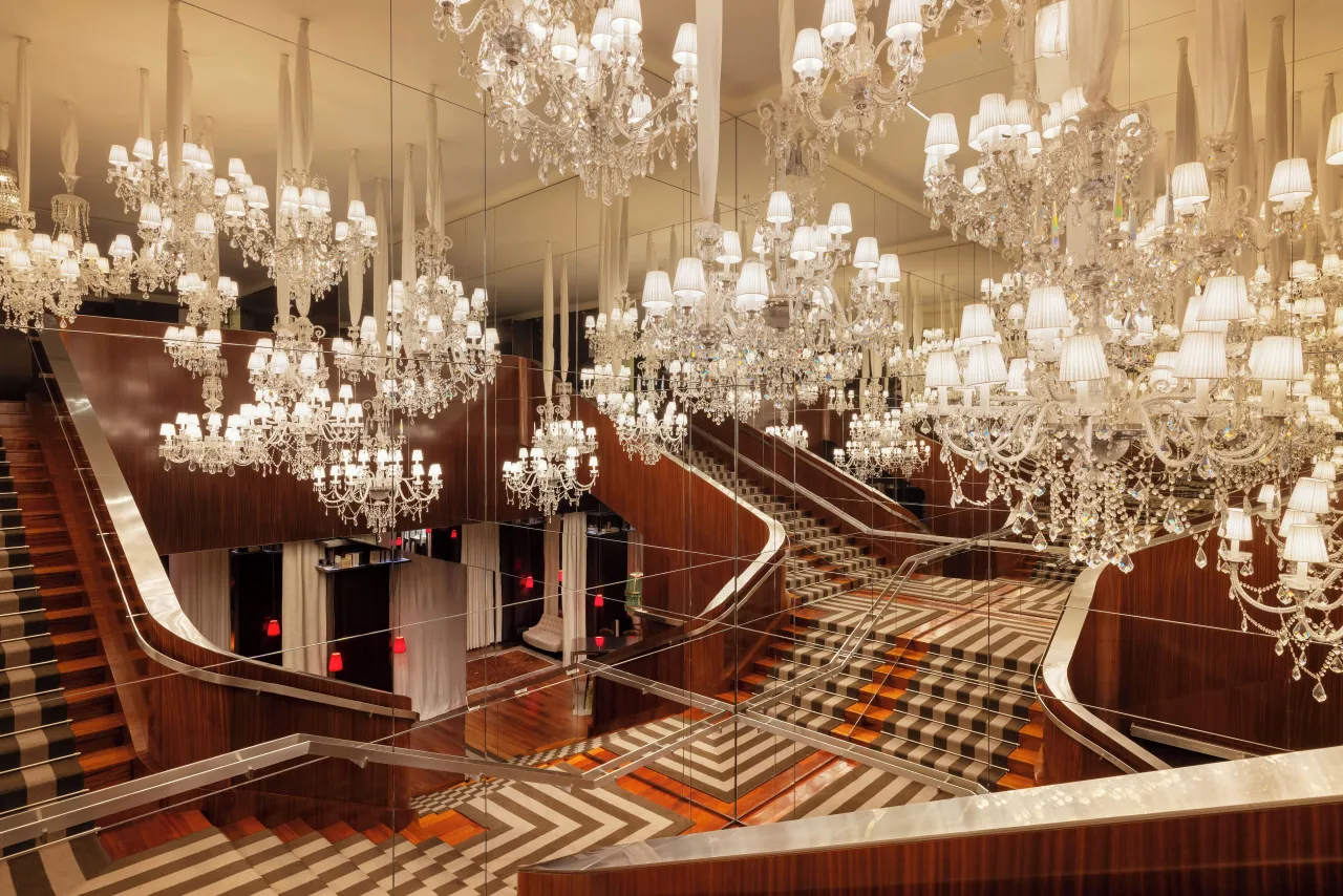 Un large escalier sous des dizaines de lustres de cristal, tapis géométrique et murs lambrissés