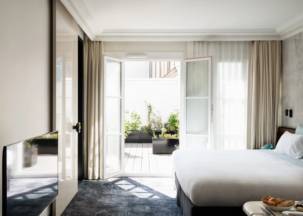 A bright bedroom with French windows open onto a terrace with plants