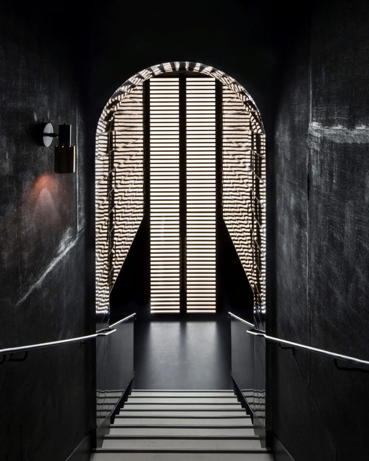 A dark stairway leading to an arched door with striped panels
