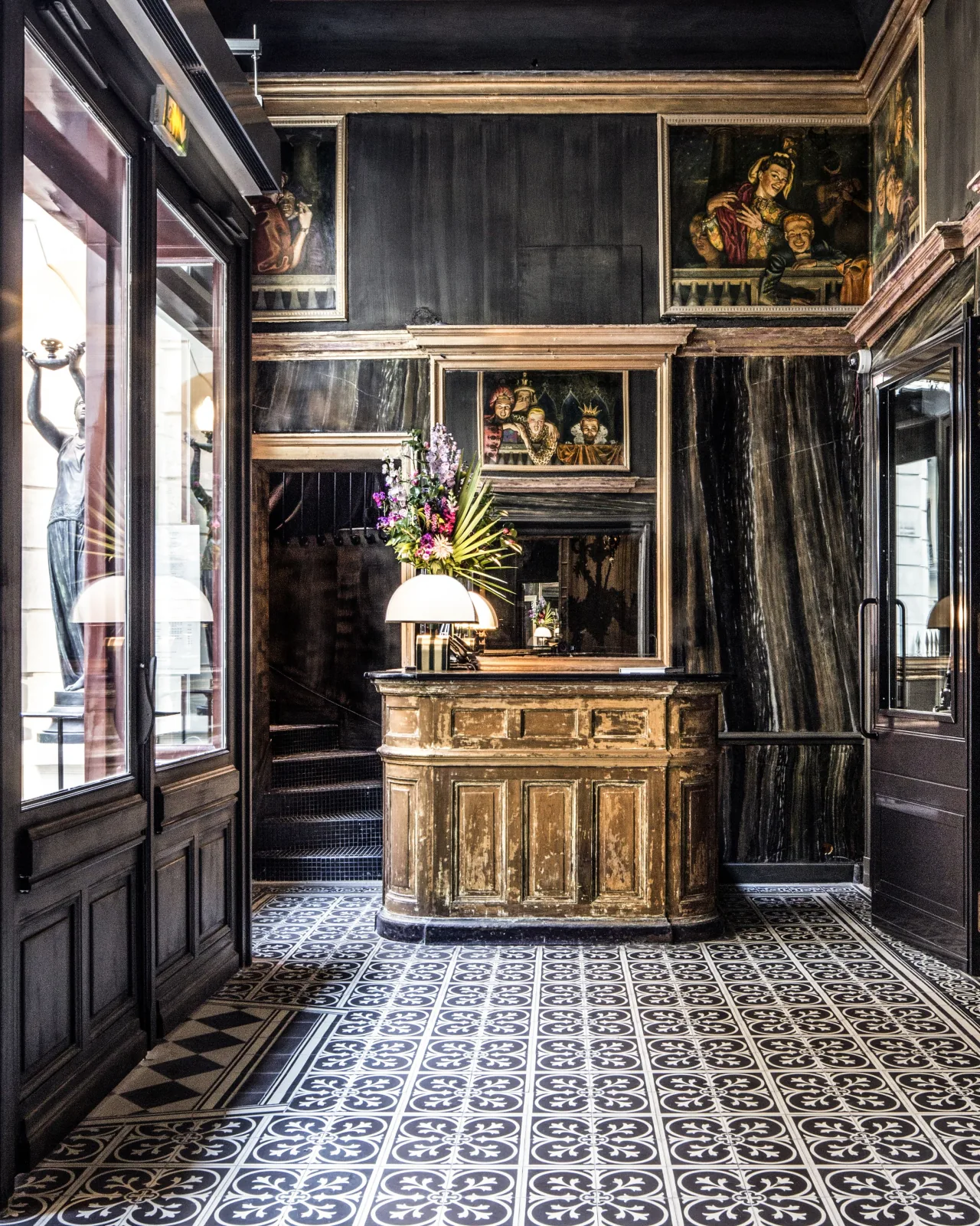 A carved wooden desk under paintings and dark panelling, on a patterned tiled floor