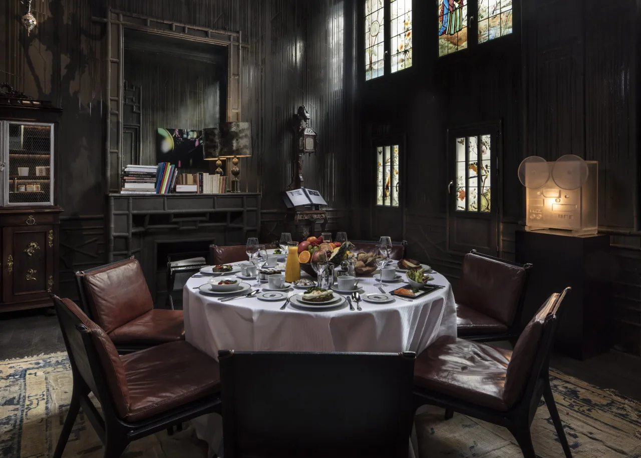 A round table set for six in a dark panelled room with books, a fireplace and stained-glass windows
