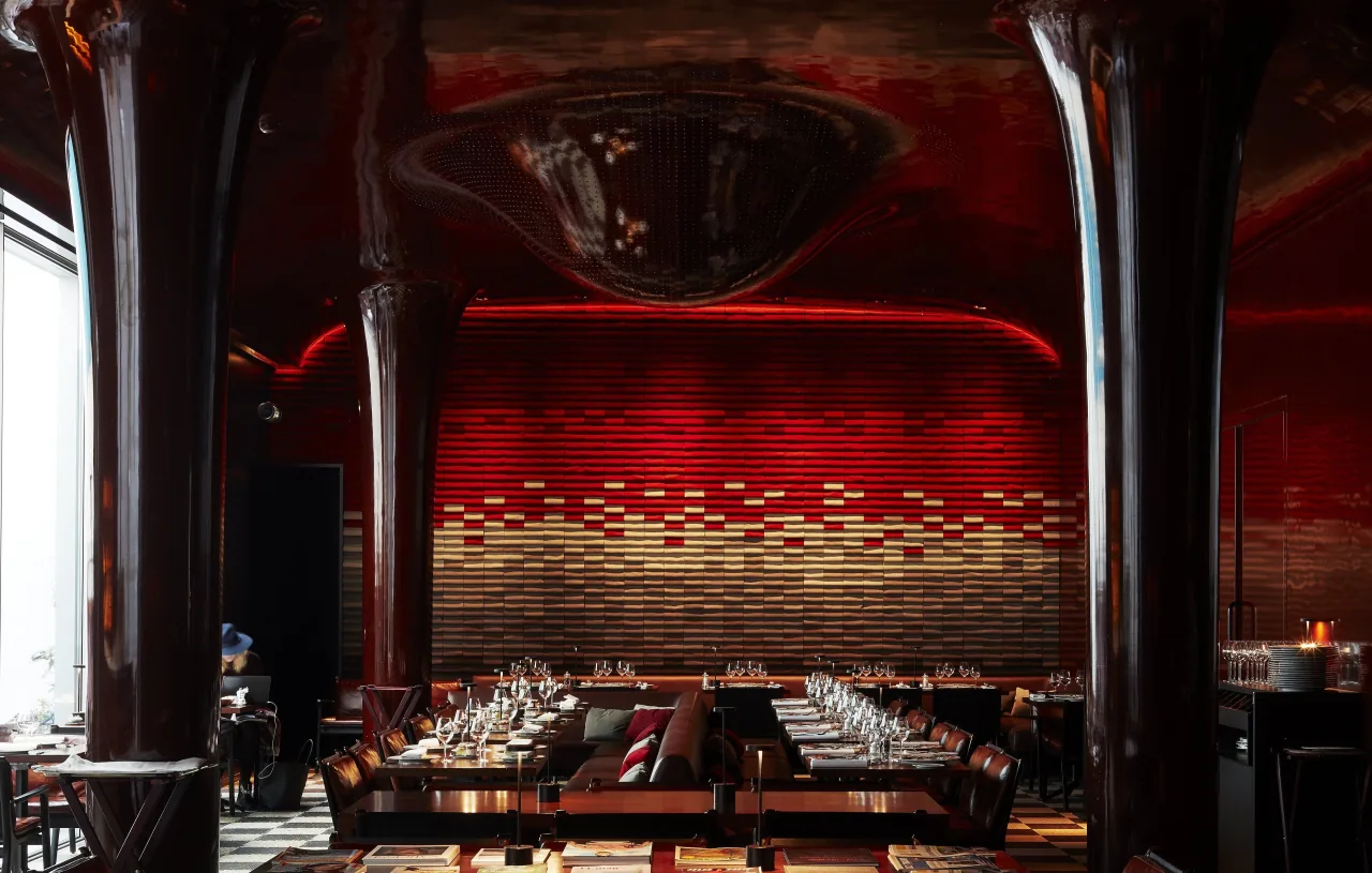 A room with red walls and long set tables between dark lacquered columns