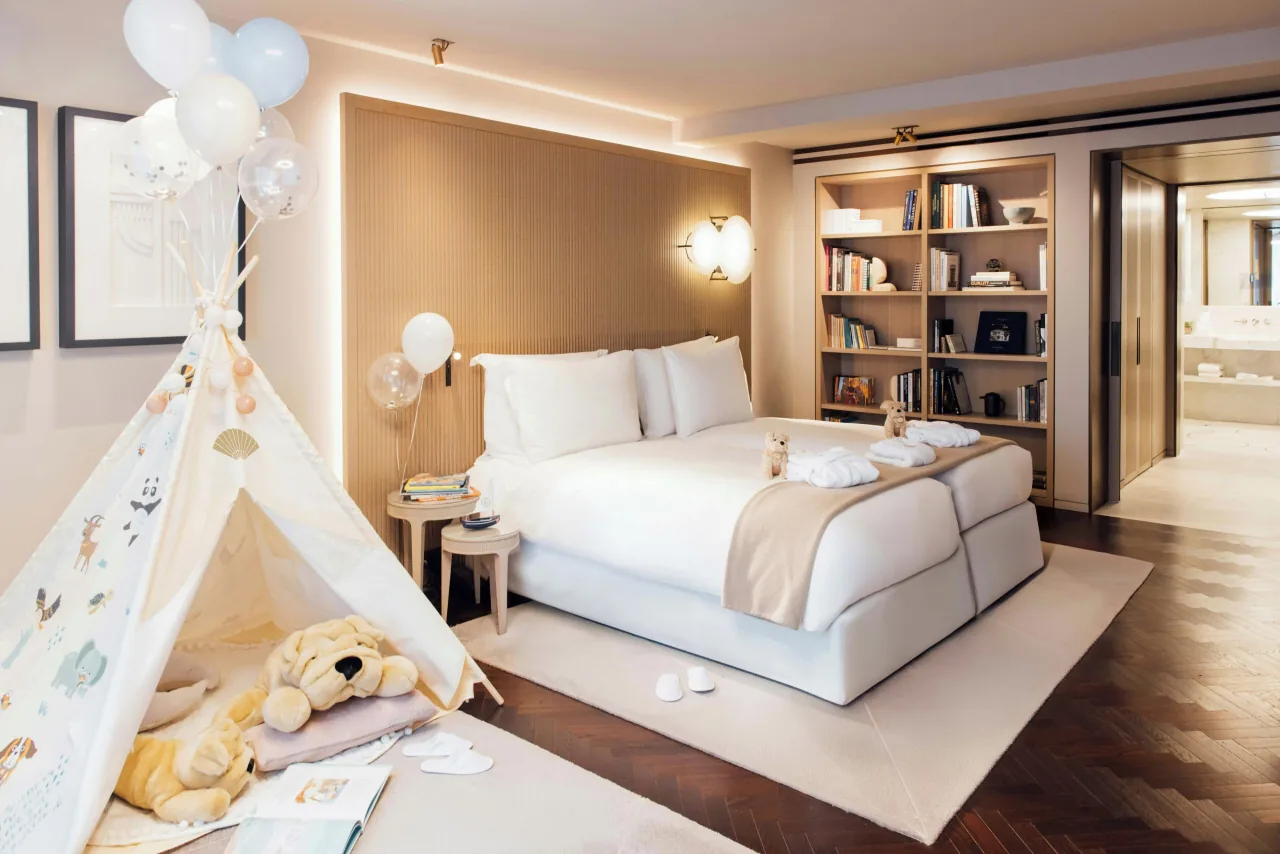 Une chambre, un lit blanc, un tipi d’enfant avec des peluches et des ballons, et des étagères de livres