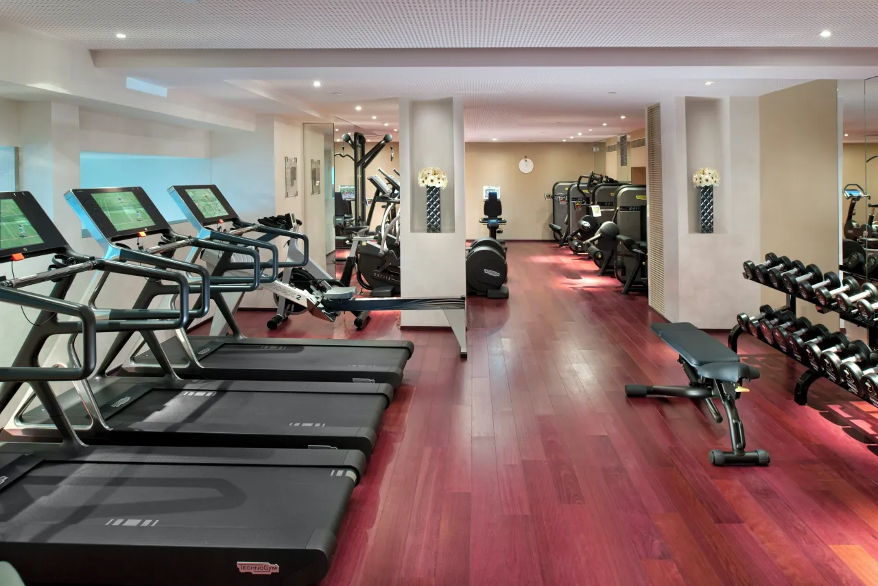 A fitness room with treadmills facing windows, a red wood floor and racks of dumbbells