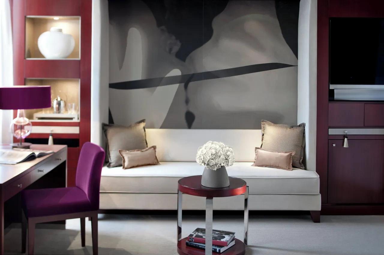 A living room with a white sofa below a large black-and-white photograph, a plum chair and a desk