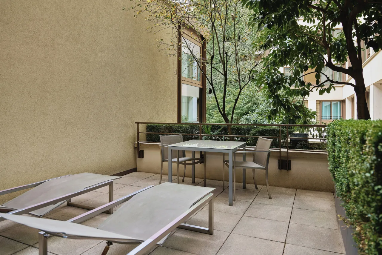 A paved terrace with two loungers and a table, a box hedge and trees of the inner garden
