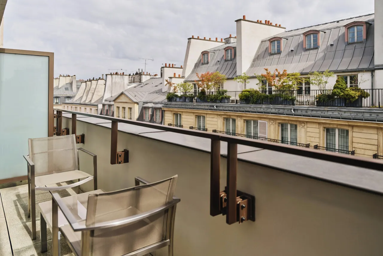 A narrow terrace with two chairs, facing Paris mansard roofs and chimneys