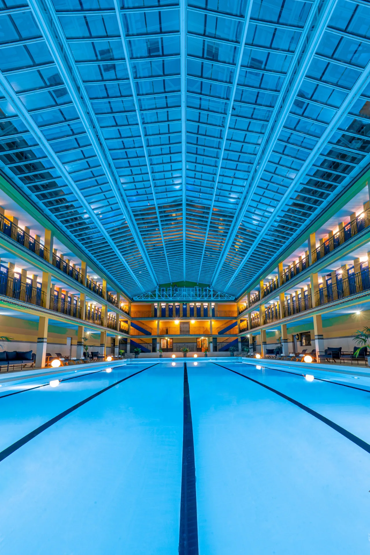 Un long bassin couvert d’une verrière, des étages de portes de cabines bleues de chaque côté