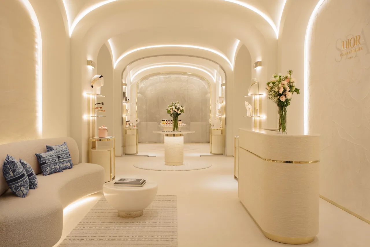 A cream vaulted spa corridor with a curved sofa and blue-patterned cushions, a rounded reception desk and white flowers