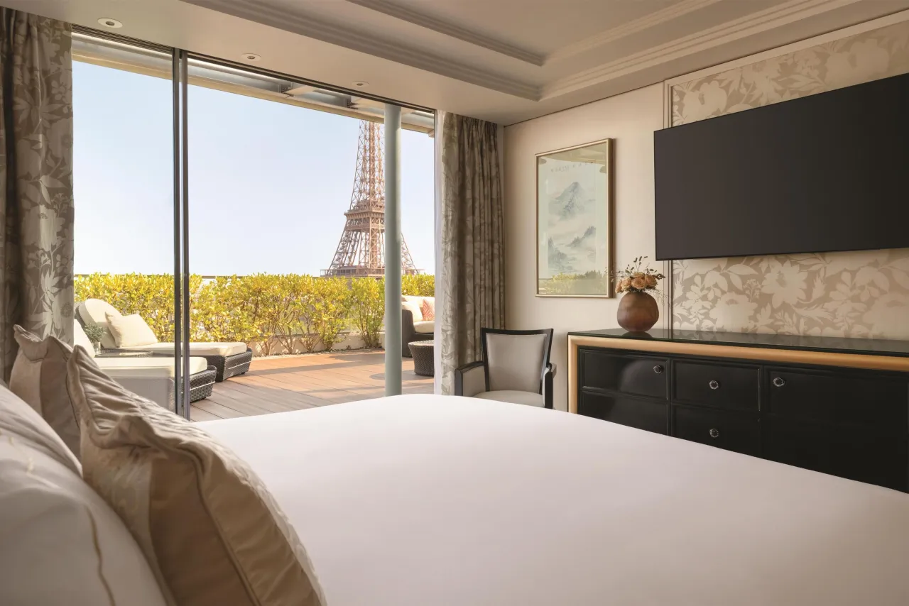 A bedroom with a large bed and a television, the Eiffel Tower visible beyond a terrace