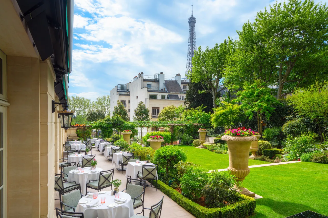 Tables laid in the hotel garden among lawns and flower beds, the Eiffel Tower above the trees